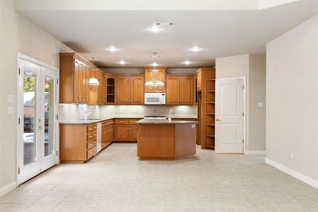 kitchen featuring pendant lighting, white appliances, a center island with sink, light stone countertops, and backsplash