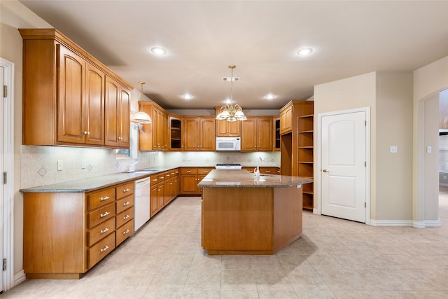 kitchen with an inviting chandelier, white appliances, sink, light stone countertops, and an island with sink