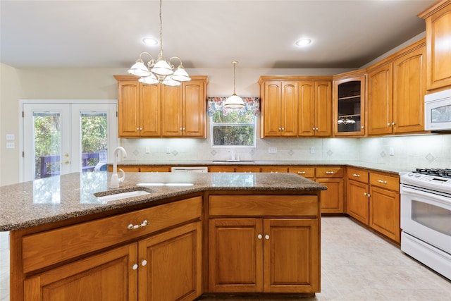 kitchen with an island with sink, hanging light fixtures, sink, white appliances, and backsplash