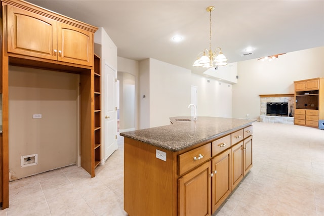 kitchen with a kitchen island with sink, an inviting chandelier, dark stone counters, decorative light fixtures, and sink