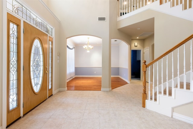 foyer with ornamental molding, light wood-type flooring, a notable chandelier, and a towering ceiling