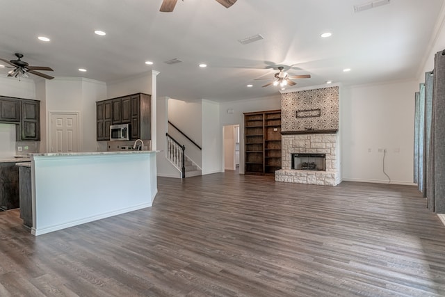 kitchen featuring ornamental molding, dark brown cabinets, ceiling fan, dark wood-type flooring, and a fireplace