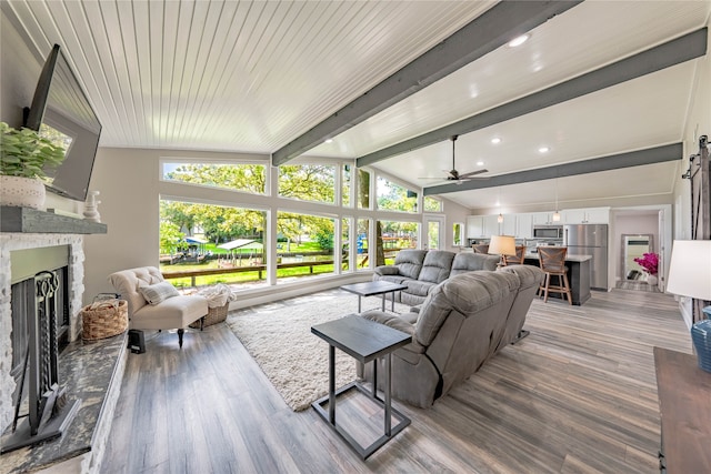 living room featuring ceiling fan, a premium fireplace, light hardwood / wood-style floors, and vaulted ceiling with beams