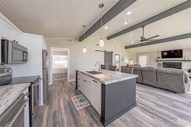 kitchen with white cabinets, a barn door, stainless steel appliances, sink, and vaulted ceiling with beams