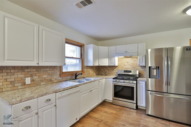 kitchen featuring appliances with stainless steel finishes, white cabinets, backsplash, light hardwood / wood-style flooring, and sink