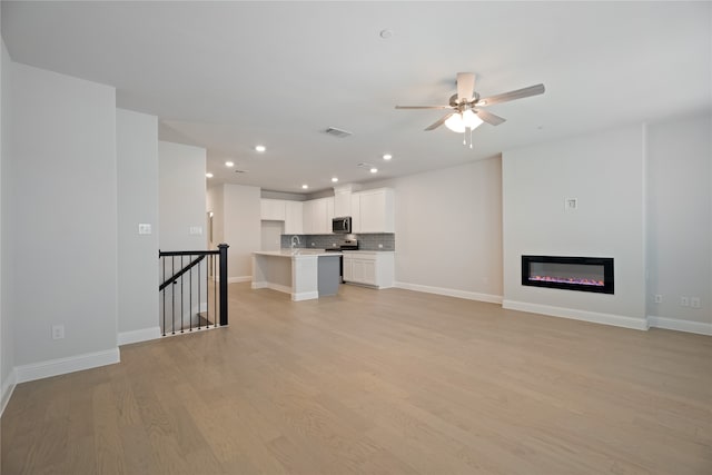 unfurnished living room with ceiling fan, sink, and light wood-type flooring