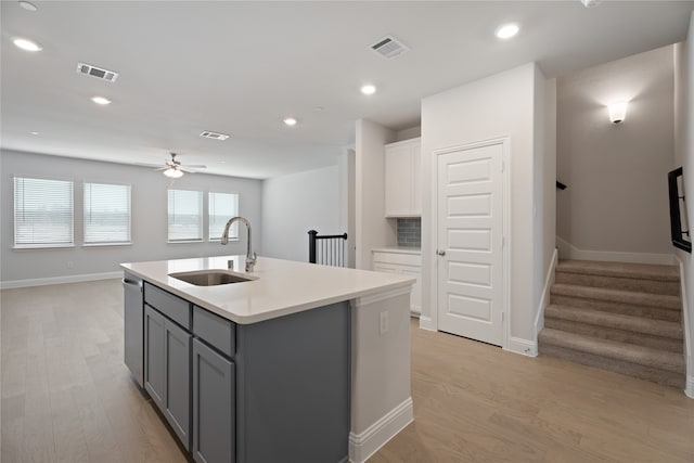 kitchen with dishwasher, sink, white cabinetry, light wood-type flooring, and a kitchen island with sink