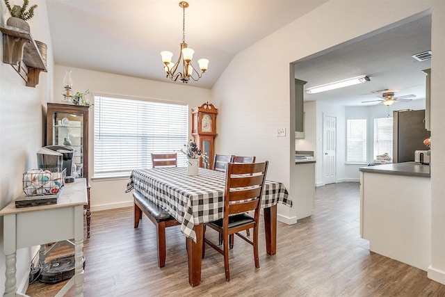 dining area with ceiling fan with notable chandelier, lofted ceiling, and wood-type flooring