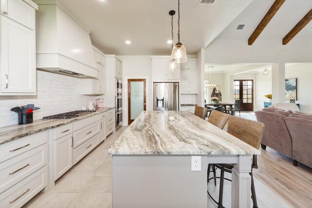 kitchen with a breakfast bar area, premium range hood, appliances with stainless steel finishes, open floor plan, and a center island