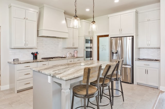 kitchen with stainless steel appliances, light stone counters, a kitchen island, white cabinetry, and premium range hood