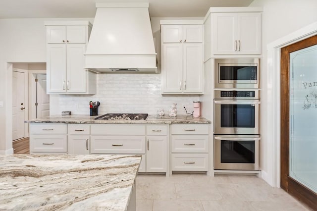 kitchen with premium range hood, light stone counters, appliances with stainless steel finishes, and white cabinets