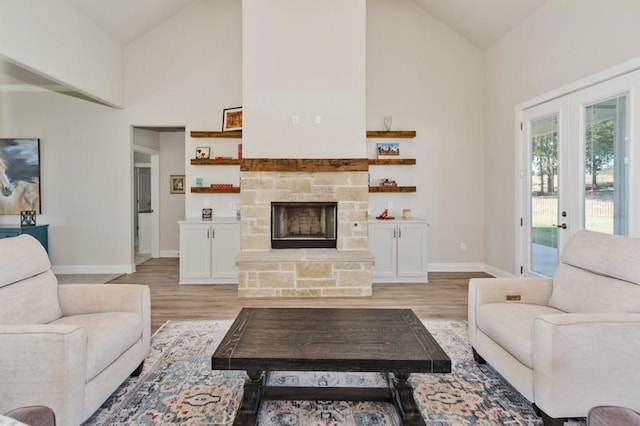 living area with light wood finished floors, a stone fireplace, french doors, and baseboards