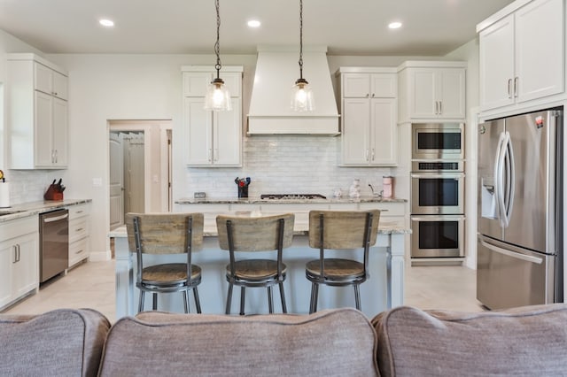 kitchen featuring light stone countertops, premium range hood, appliances with stainless steel finishes, a kitchen bar, and open floor plan