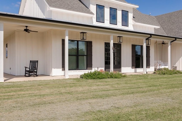 back of house with a yard, board and batten siding, a ceiling fan, and roof with shingles