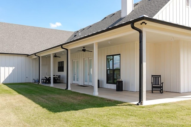 rear view of house with a ceiling fan, roof with shingles, a yard, a patio area, and board and batten siding