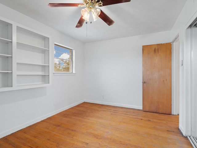 spare room with light wood-type flooring, built in shelves, and ceiling fan