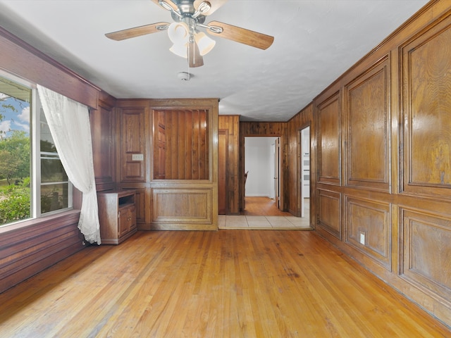 interior space featuring light hardwood / wood-style flooring, wood walls, and ceiling fan