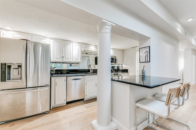 kitchen with white cabinetry, ornate columns, stainless steel appliances, and light hardwood / wood-style floors