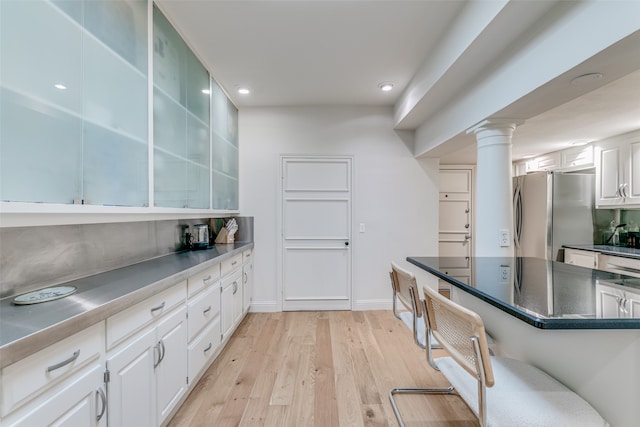 kitchen with light wood-type flooring, stainless steel refrigerator, a kitchen bar, ornate columns, and white cabinets