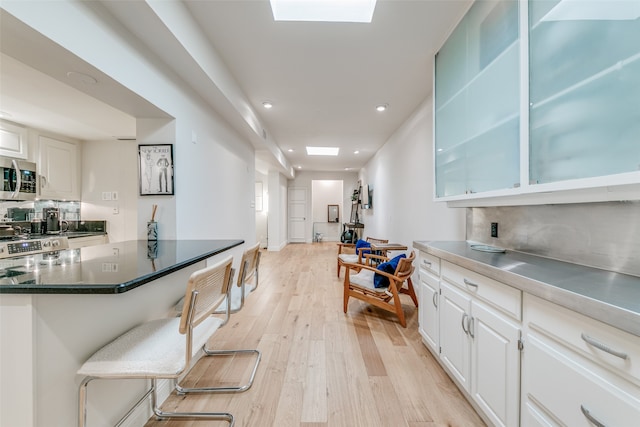 kitchen featuring a breakfast bar area, light hardwood / wood-style flooring, backsplash, a skylight, and white cabinets