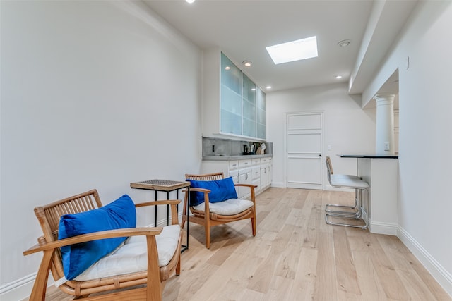 living area with light hardwood / wood-style floors, ornate columns, and a skylight