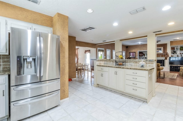 kitchen featuring tasteful backsplash, stainless steel refrigerator with ice dispenser, light stone countertops, and white cabinets