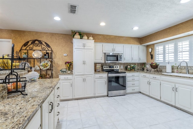 kitchen with sink, stainless steel appliances, tasteful backsplash, light stone countertops, and white cabinets