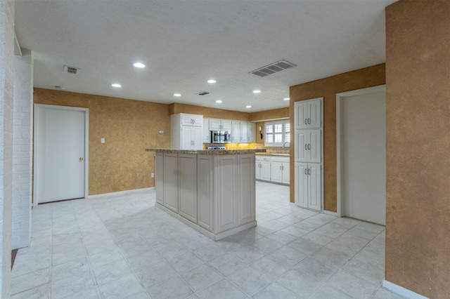 kitchen with light stone counters, a center island, sink, and white cabinets