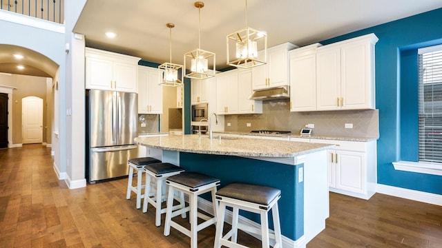 kitchen featuring a kitchen island with sink, white cabinetry, stainless steel appliances, and hanging light fixtures