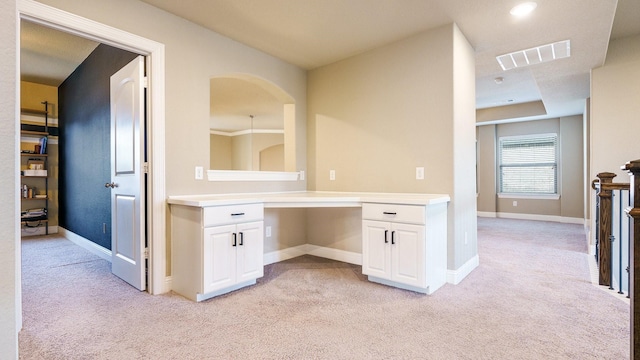 interior space featuring white cabinetry, light colored carpet, and built in desk