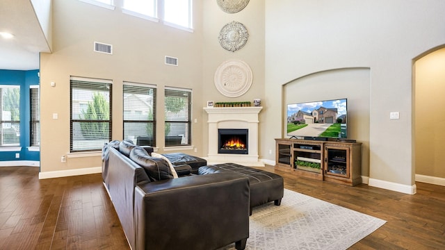 living room featuring a towering ceiling, dark hardwood / wood-style floors, and a healthy amount of sunlight