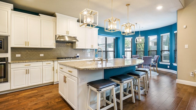 kitchen with decorative light fixtures, sink, white cabinetry, and an island with sink