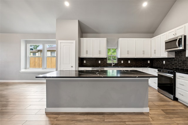 kitchen with lofted ceiling, a kitchen island, stainless steel appliances, and white cabinets