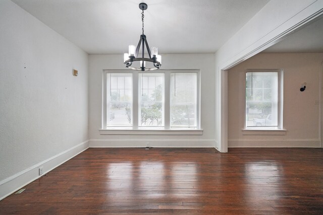 unfurnished dining area with a healthy amount of sunlight, a notable chandelier, and dark hardwood / wood-style flooring