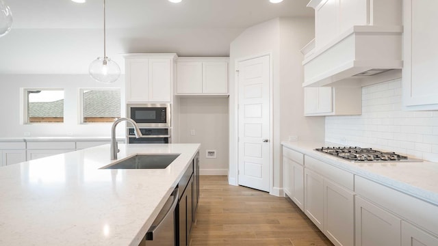 kitchen with light stone countertops, hanging light fixtures, stainless steel appliances, and custom exhaust hood