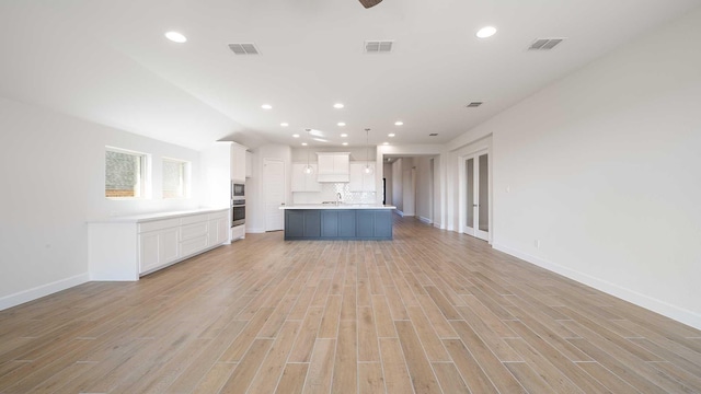 kitchen featuring white cabinetry, light hardwood / wood-style floors, backsplash, a kitchen island with sink, and pendant lighting