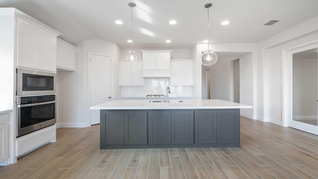 kitchen with white cabinetry, an island with sink, hanging light fixtures, stainless steel oven, and built in microwave