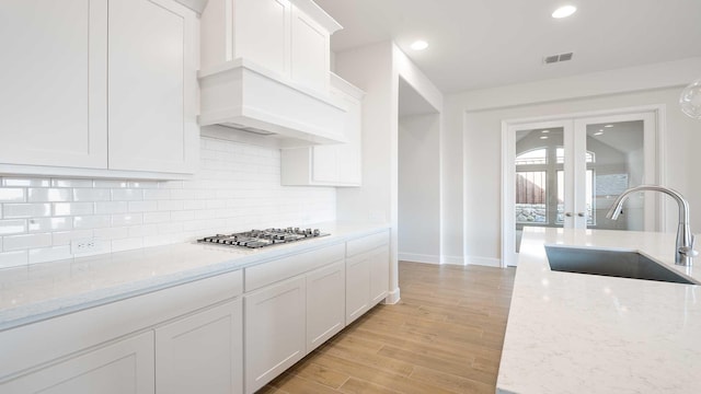 kitchen with stainless steel gas stovetop, white cabinetry, light stone counters, and sink