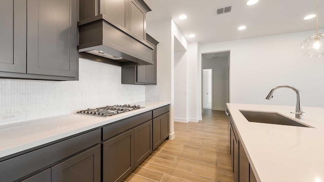 kitchen with sink, stainless steel gas cooktop, backsplash, premium range hood, and pendant lighting