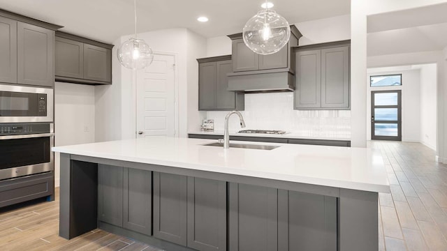 kitchen featuring pendant lighting, a kitchen island with sink, sink, gray cabinets, and stainless steel appliances