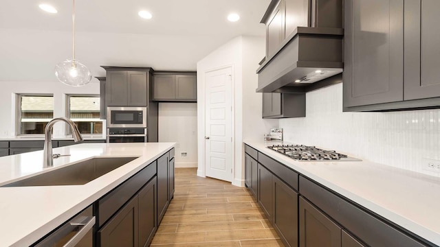 kitchen featuring decorative backsplash, ventilation hood, stainless steel appliances, sink, and hanging light fixtures