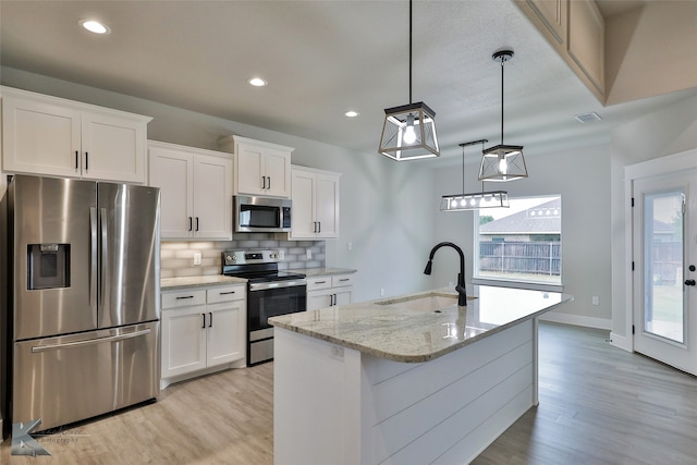 kitchen with white cabinets, light wood-type flooring, stainless steel appliances, sink, and a kitchen island with sink