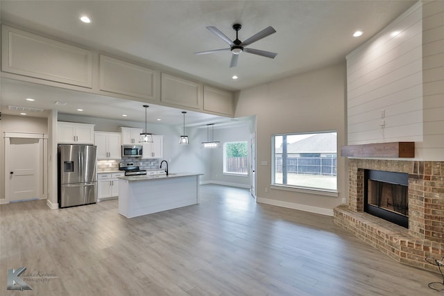 kitchen with a fireplace, light hardwood / wood-style flooring, stainless steel appliances, white cabinetry, and ceiling fan