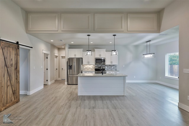 kitchen with stainless steel appliances, a barn door, light stone counters, light wood-type flooring, and white cabinets