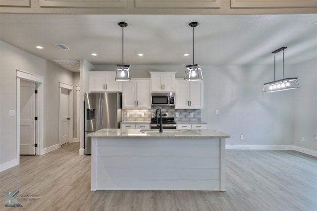 kitchen with decorative light fixtures, white cabinets, stainless steel appliances, and light wood-type flooring