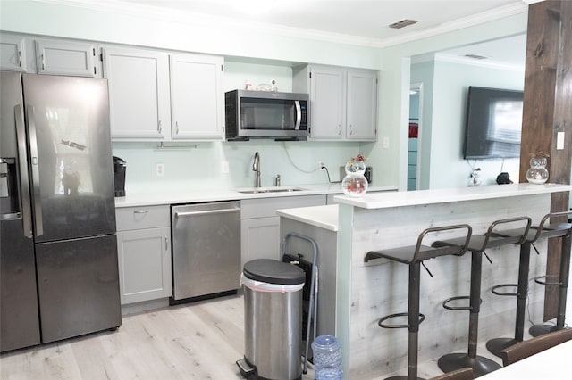 kitchen featuring crown molding, sink, light hardwood / wood-style flooring, appliances with stainless steel finishes, and a kitchen bar