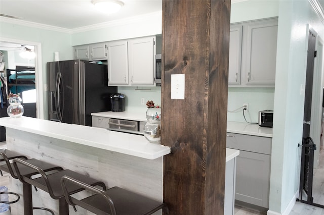 kitchen featuring crown molding, gray cabinets, light wood-type flooring, appliances with stainless steel finishes, and a breakfast bar area