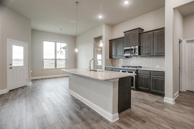 kitchen featuring stainless steel appliances, sink, light stone counters, tasteful backsplash, and a kitchen island with sink