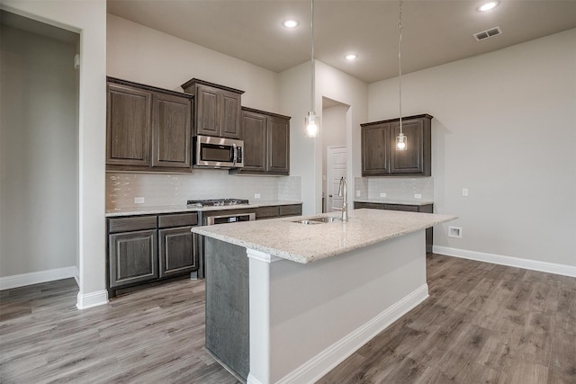 kitchen featuring light stone counters, stainless steel appliances, backsplash, and an island with sink