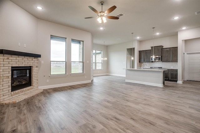 unfurnished living room with sink, a fireplace, ceiling fan, and light hardwood / wood-style floors